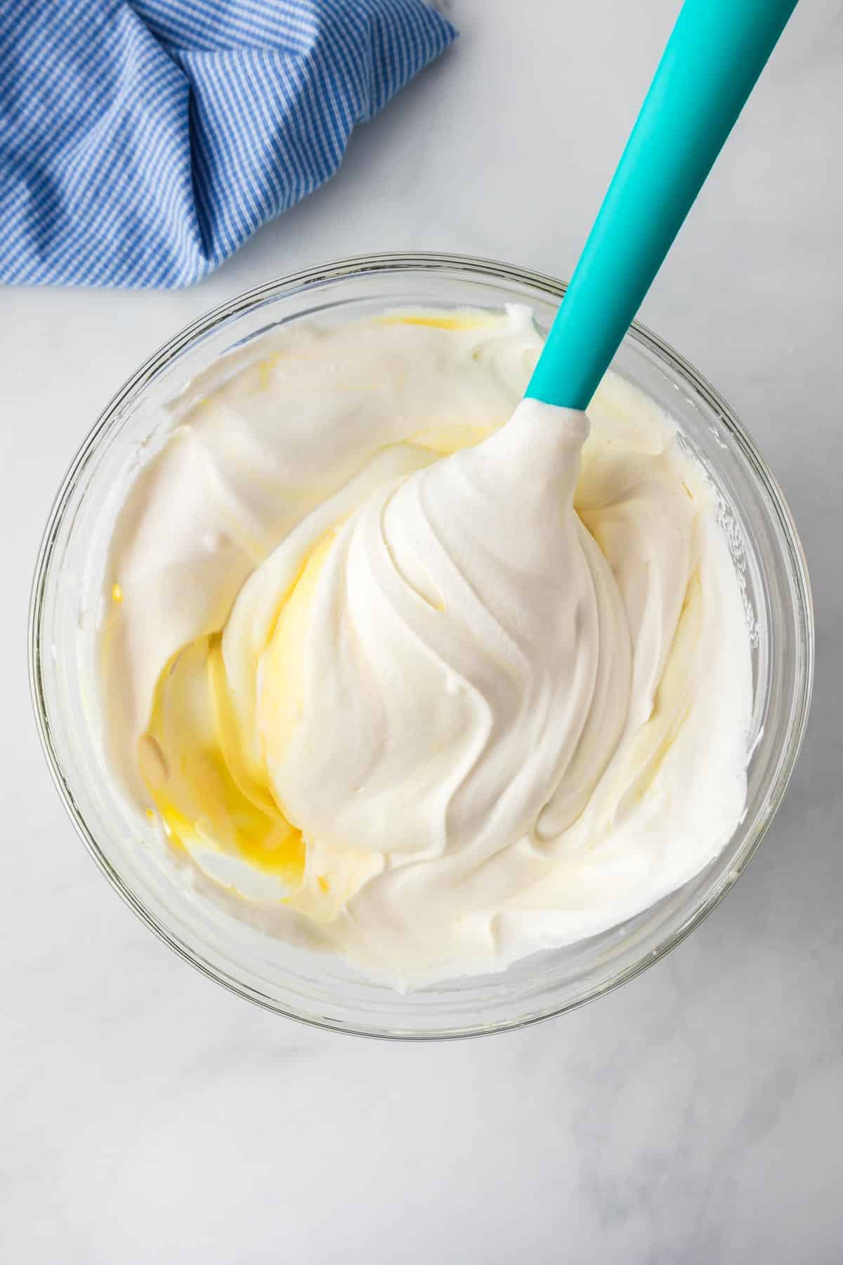 A spatula in a glass bowl mixing whipped topping into the banana pudding mixture.