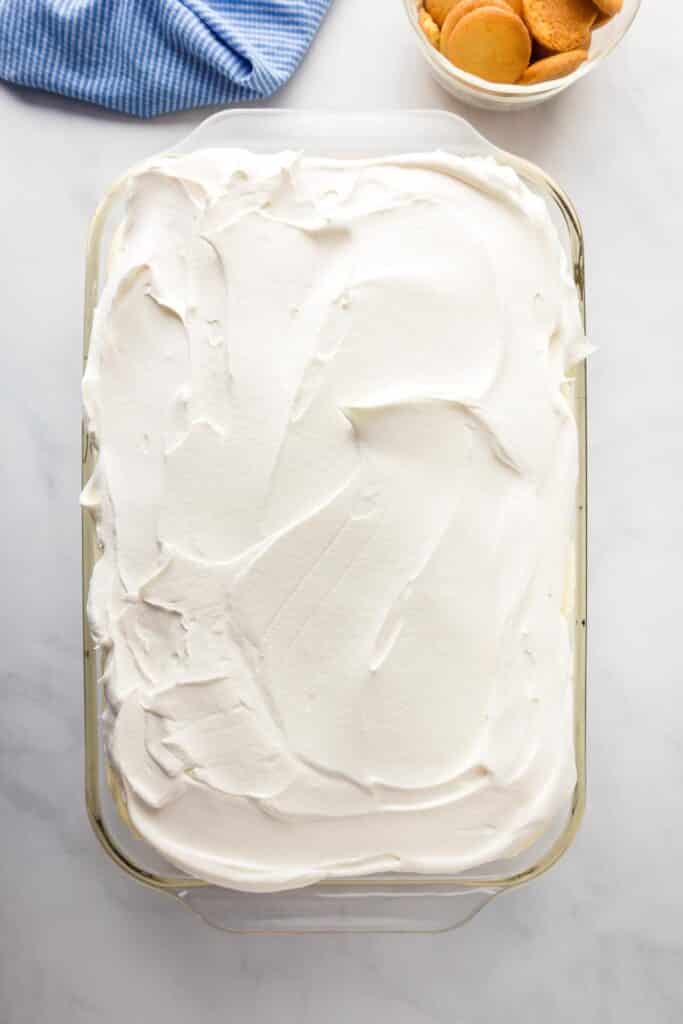 A rectangular glass dish filled with banana pudding poke cake topped with a whipped cream frosting.