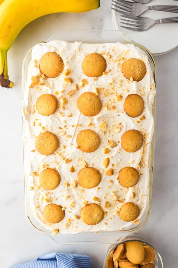 Banana pudding poke cake in a glass casserole dish from above topped with a whipped cream frosting and vanilla wafers.