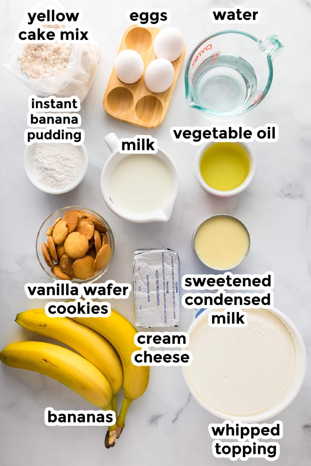 Ingredients for a banana pudding poke cake on a counter with text labels,.