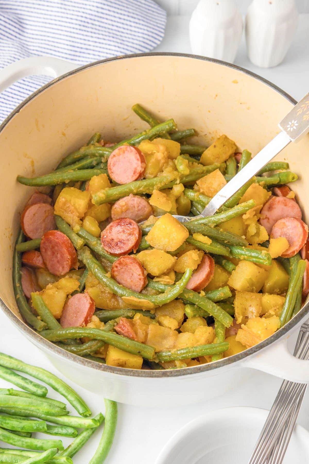 A pot containing green beans, potato chunks, and sliced sausage mixed together.