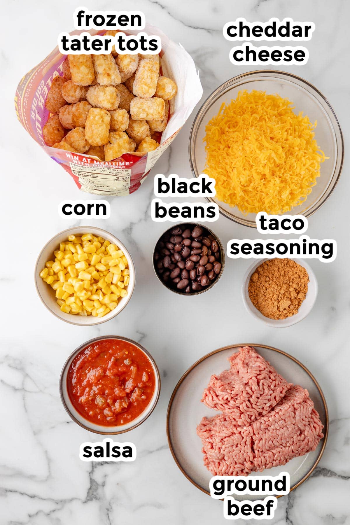 Ingredients for a taco tater tot casserole in bowls on a counter with text labels.