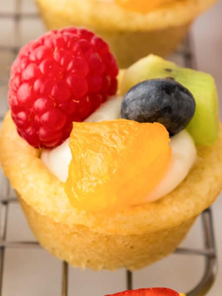 Mini fruit pizza cookie cup filled with cheesecake filling and topped with fresh fruit.