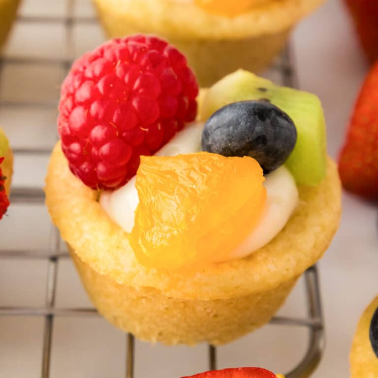 Mini fruit pizza cookie cup filled with cheesecake filling and topped with fresh fruit.