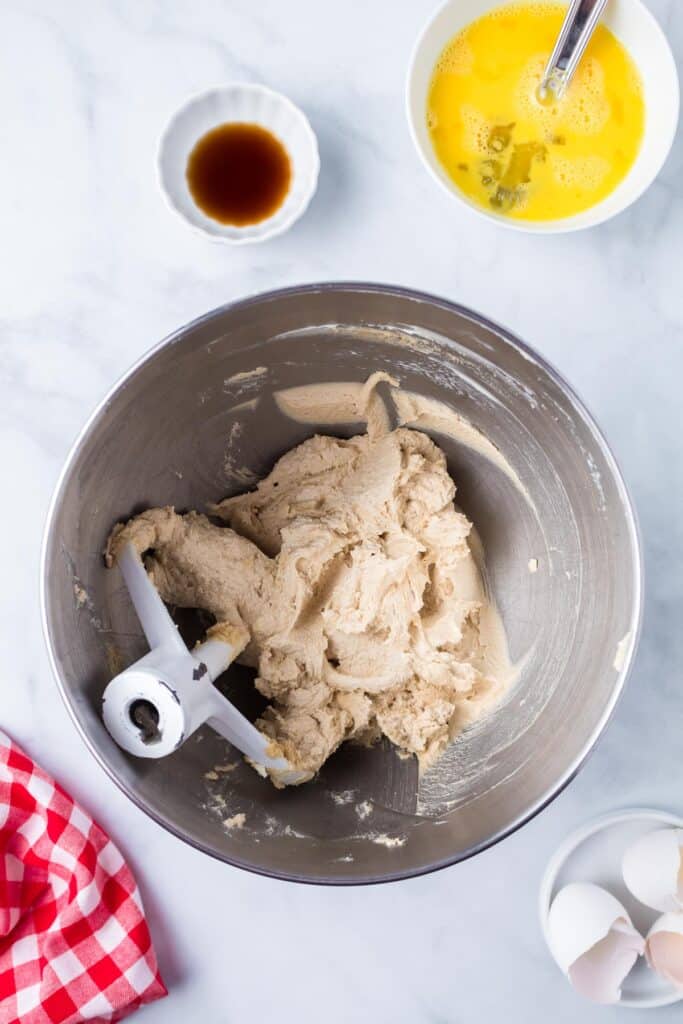 A mixing bowl with a cookie dough being mixed with a beaten egg in a bowl and vanilla on a counter nearby.