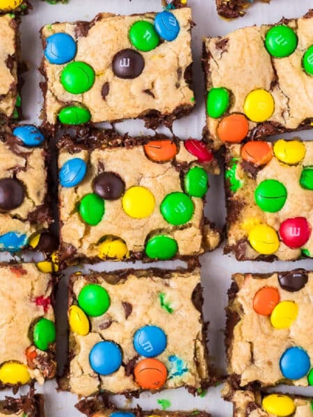 Square view of M&M cookie bars topped with colorful chocolate candies sliced from above.