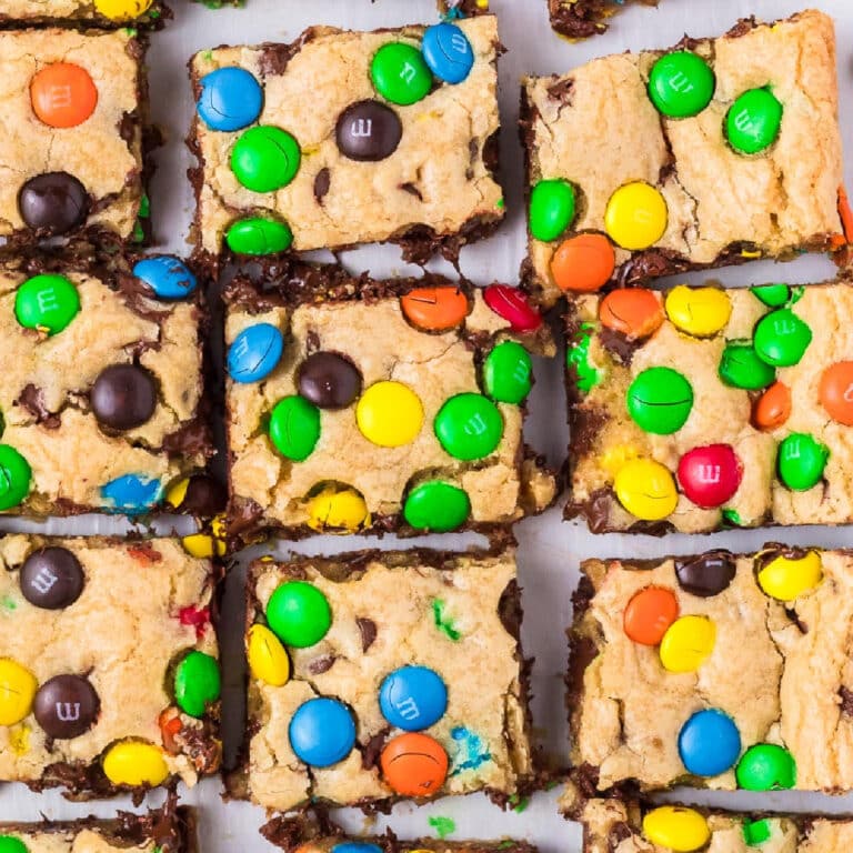 Square view of M&M cookie bars topped with colorful chocolate candies sliced from above.