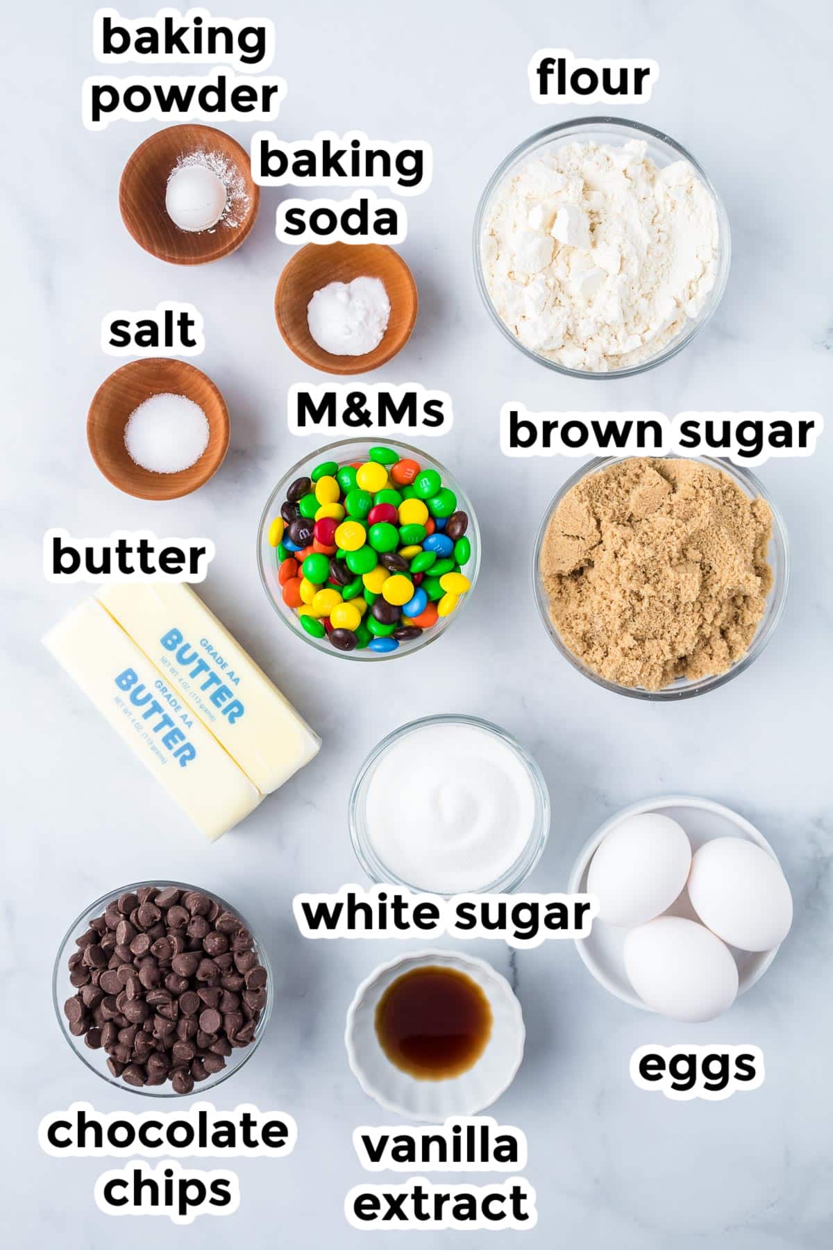 Ingredients for M&M cookie bars on a counter in bowls with text labels.