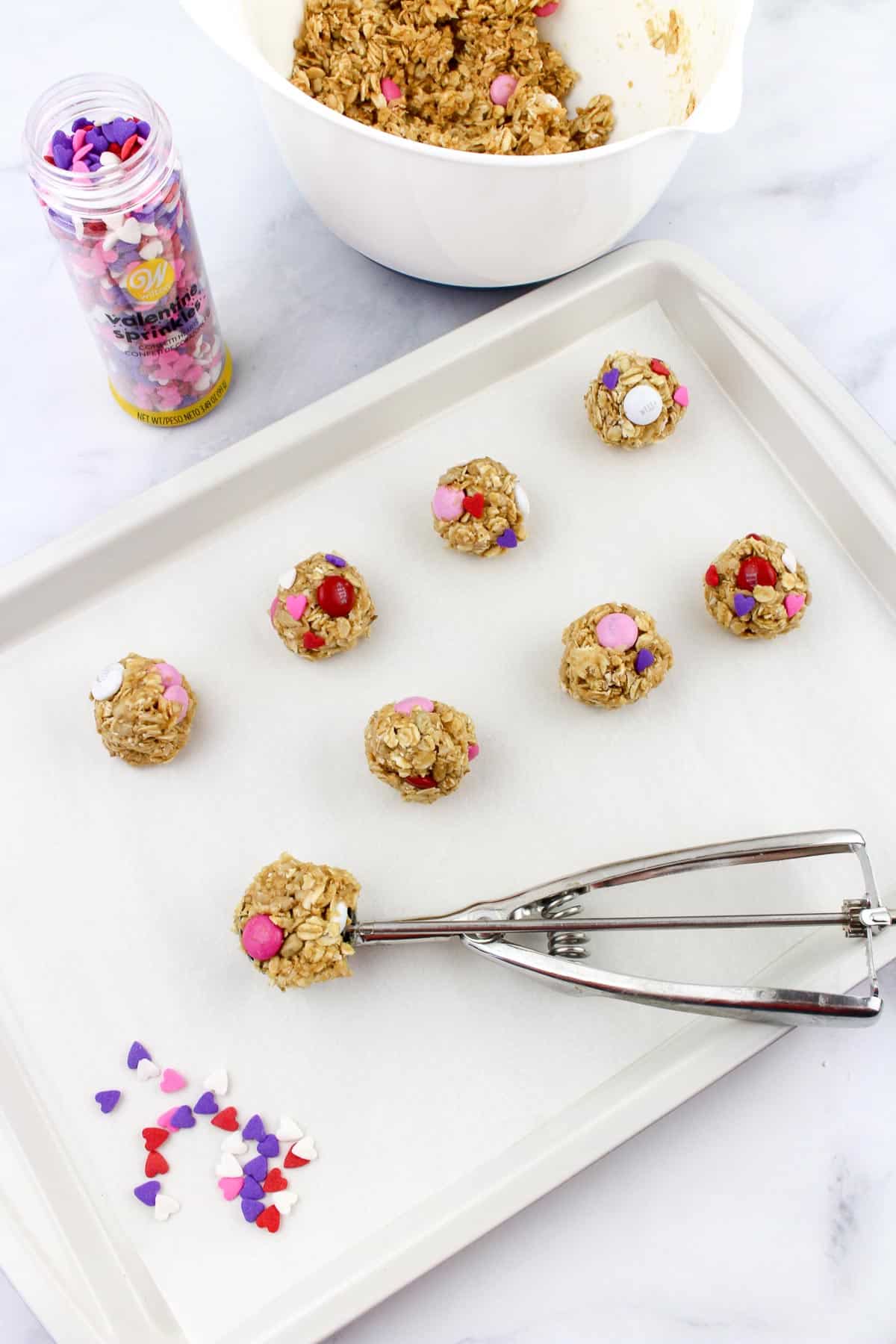 Valentine's Day snack bites being scooped with a cookie scoop and placed on a baking sheet.