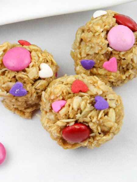 Three oat-based energy bites decorated with pink, red, and white candy and heart-shaped sprinkles.