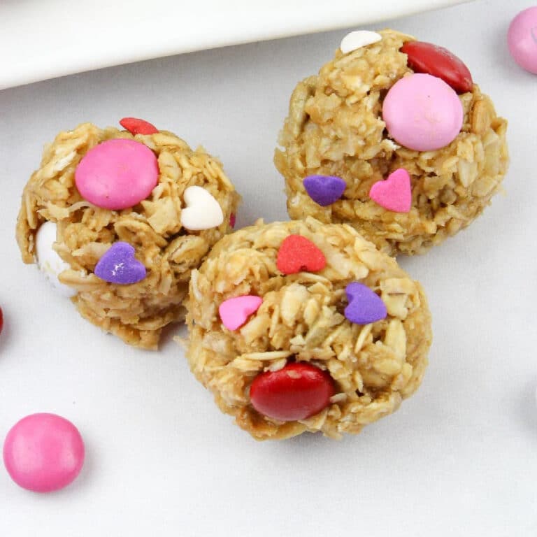 Three oat-based energy bites decorated with pink, red, and white candy and heart-shaped sprinkles.