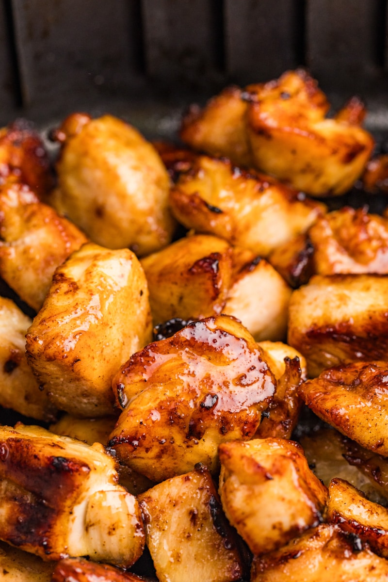 Close-up of grilled chicken pieces with a golden brown, glazed surface, arranged on a grill.