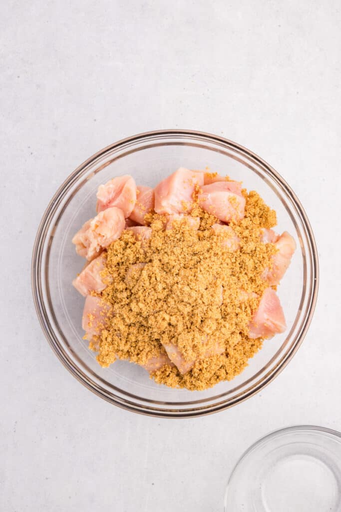 Chunks of raw chicken breast covered with brown sugar and seasoning before mixing.