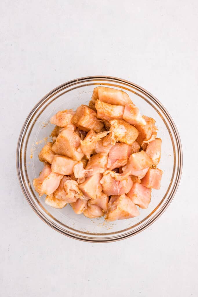 A bowl filled with raw, cubed chicken pieces mixed with with spices and brown sugar.