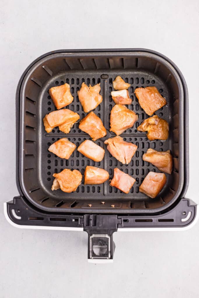 Chunks of raw chicken bites arranged inside an air fryer basket.