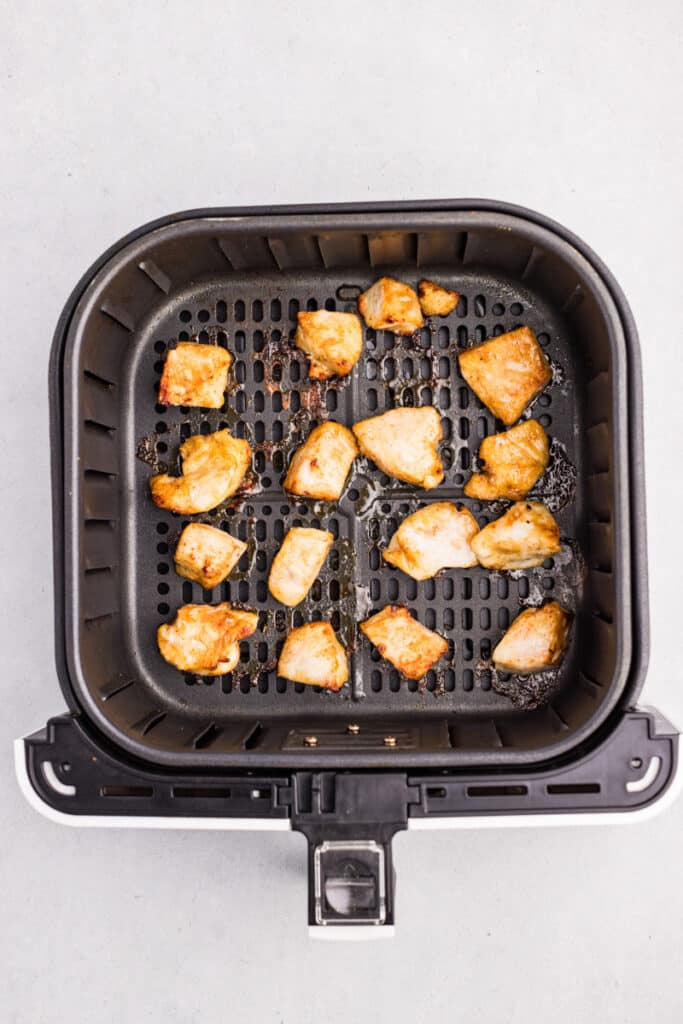 Chunks of half cooked air fryer chicken bites in an air fryer basket.