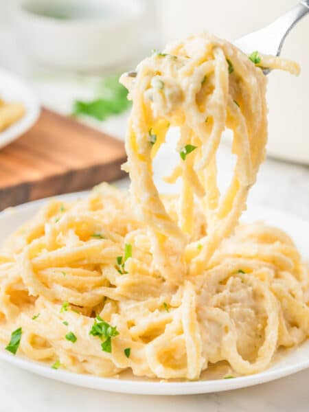Square view of a fork lifting a portion of creamy linguini alfredo from a plate.