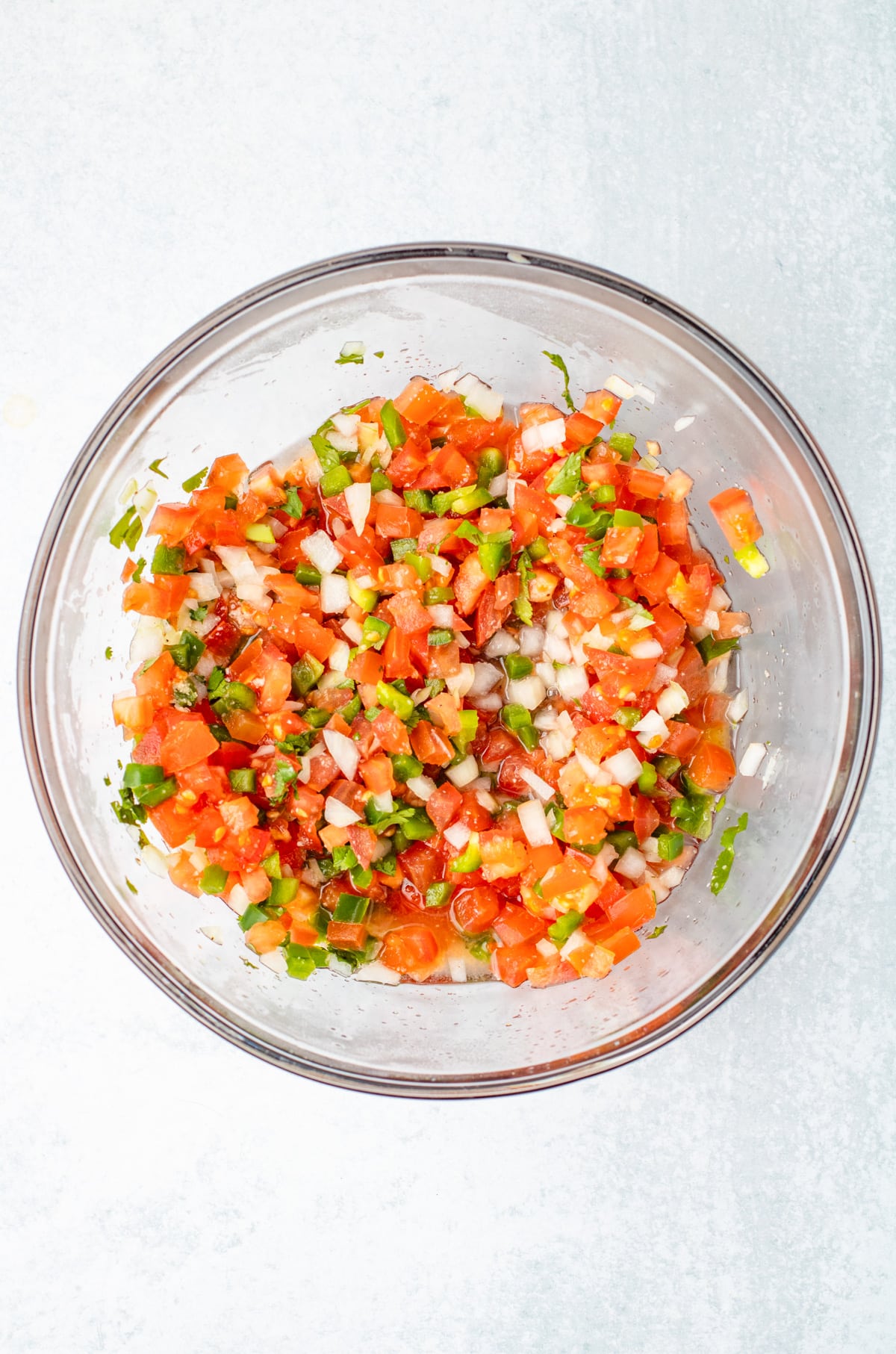 A bowl of freshly mixed pico de gallo with diced tomatoes, onions, cilantro, and green peppers mixed together.