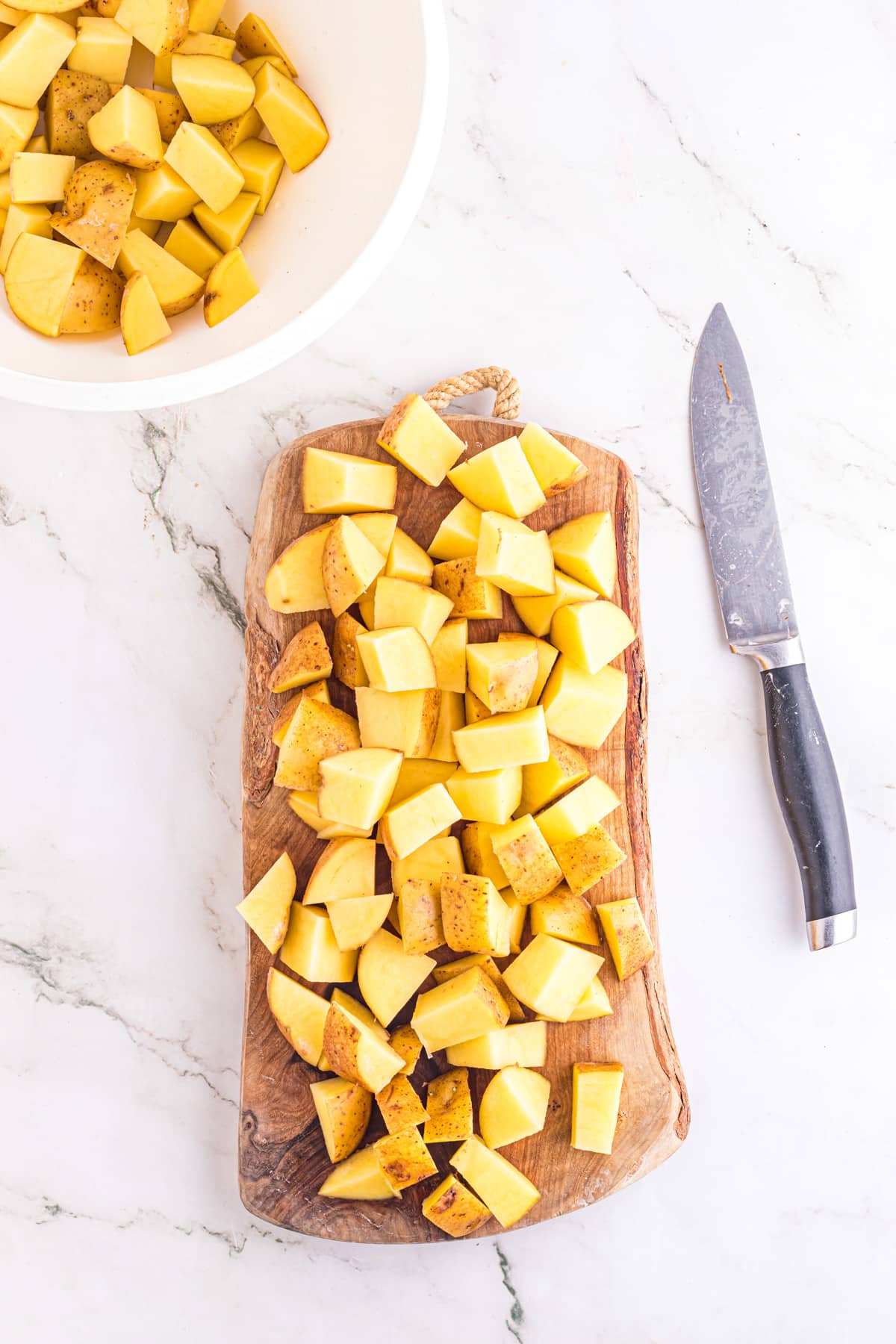 Chopped yellow potatoes on a cutting board being switched to a bowl for seasoning for pork tenderloin and potatoes.