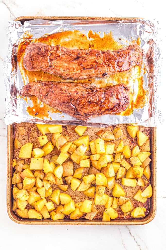 Roasted pork tenderloins and potatoes on a half foil-lined baking sheet with the potatoes on the non-lined pan side.