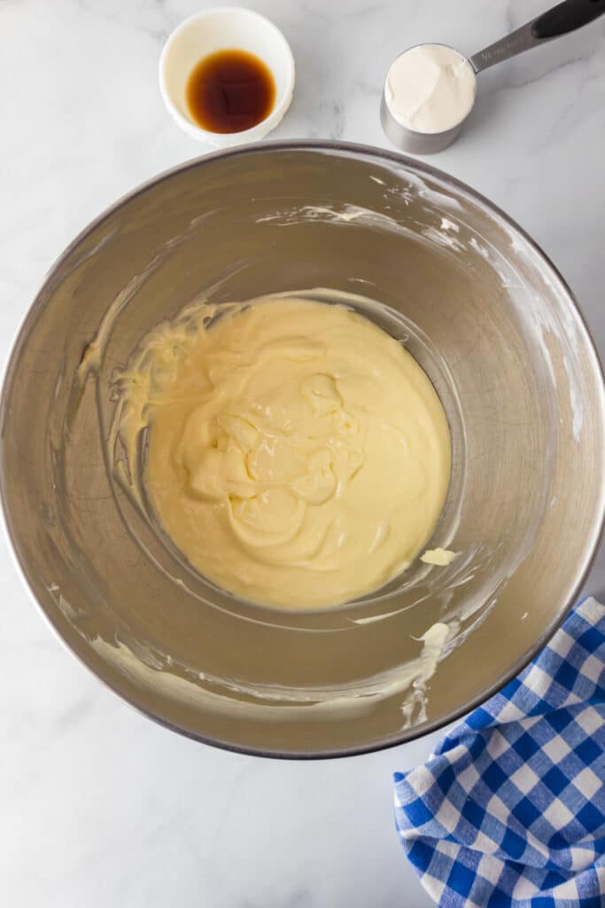 A cream cheese egg mixture after mixing with sugar with vanilla and sour cream nearby on the counter.