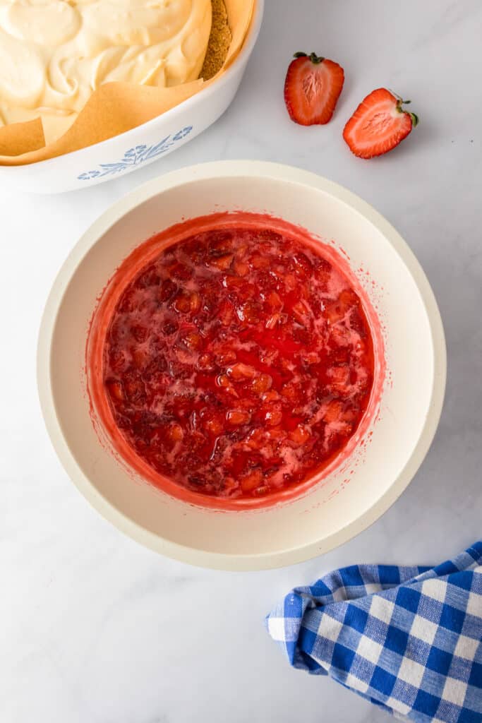 A bowl of strawberry filling next to a dish full of the strawberry cheesecake bars.