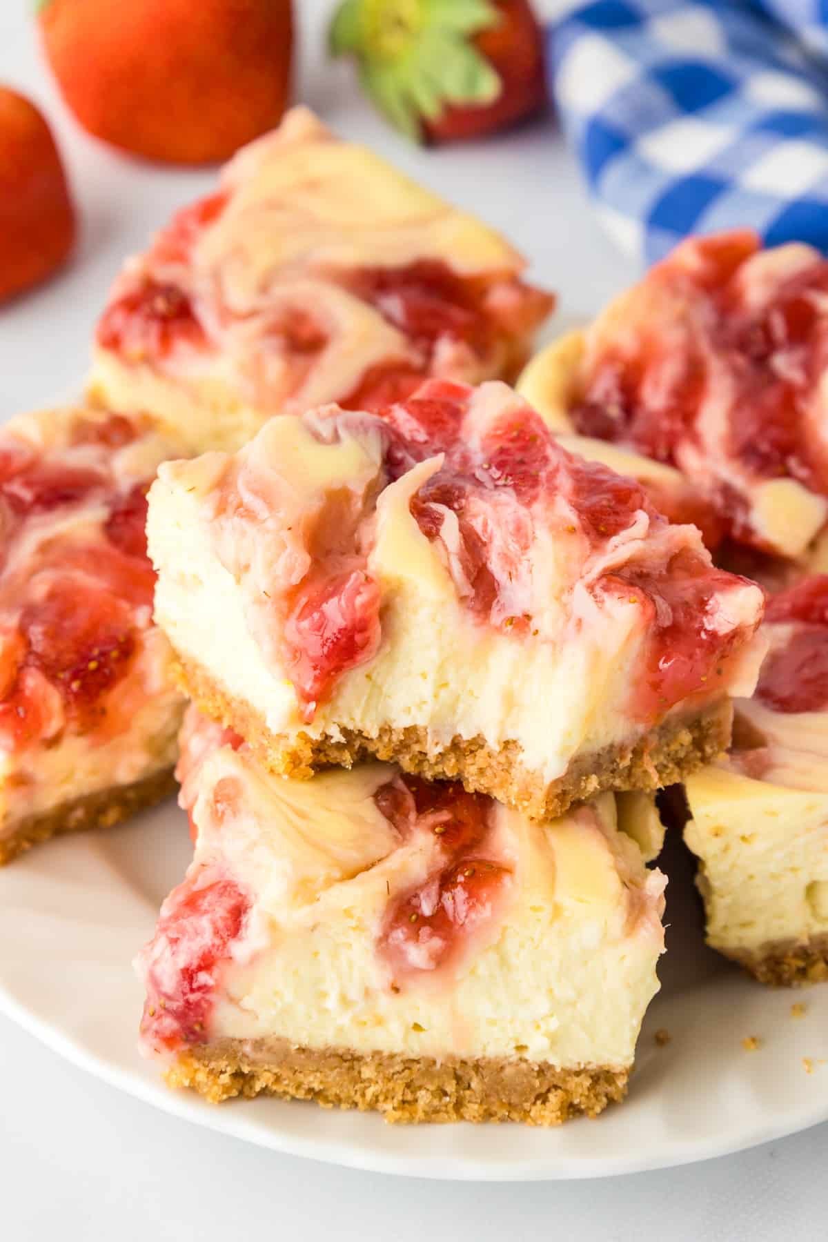 A stack of strawberry swirled cheesecake bars with a graham cracker crust on a plate stacked with the top bar missing a bite.