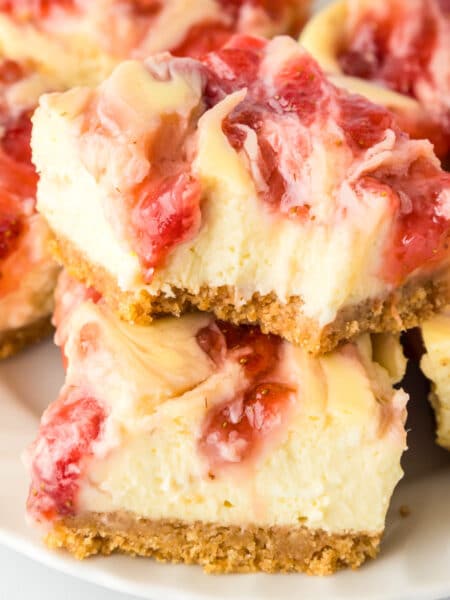 Square close-up of strawberry swirl cheesecake bars stacked on a platter with the top bar missing a bite.