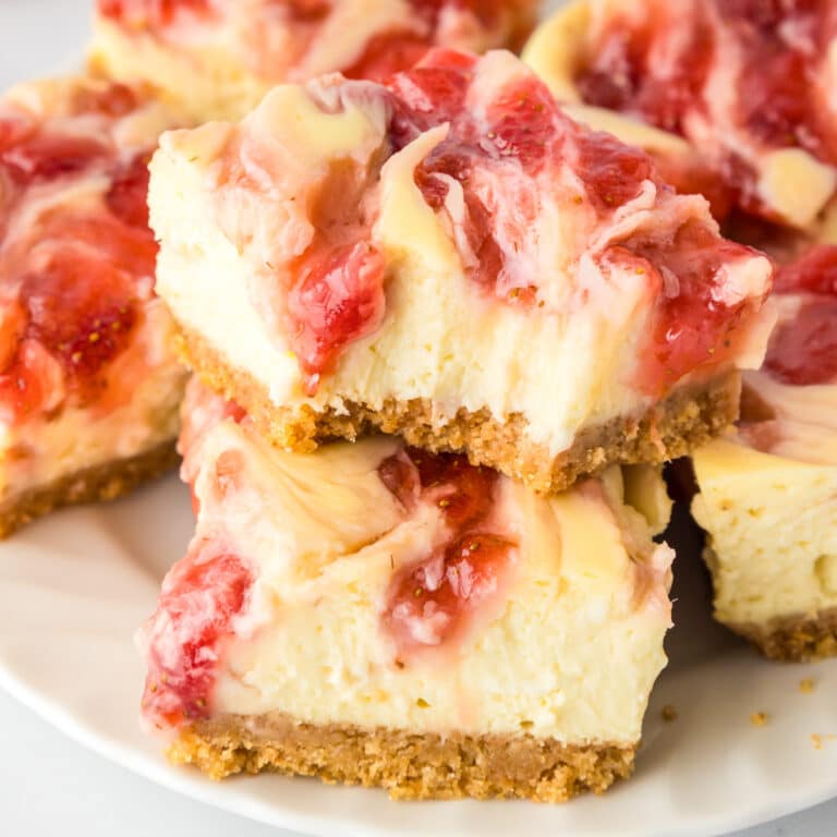 Square close-up of strawberry swirl cheesecake bars stacked on a platter with the top bar missing a bite.