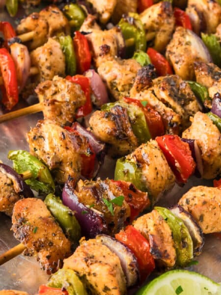 Close up square view of chicken fajita skewers piled on a serving platter.
