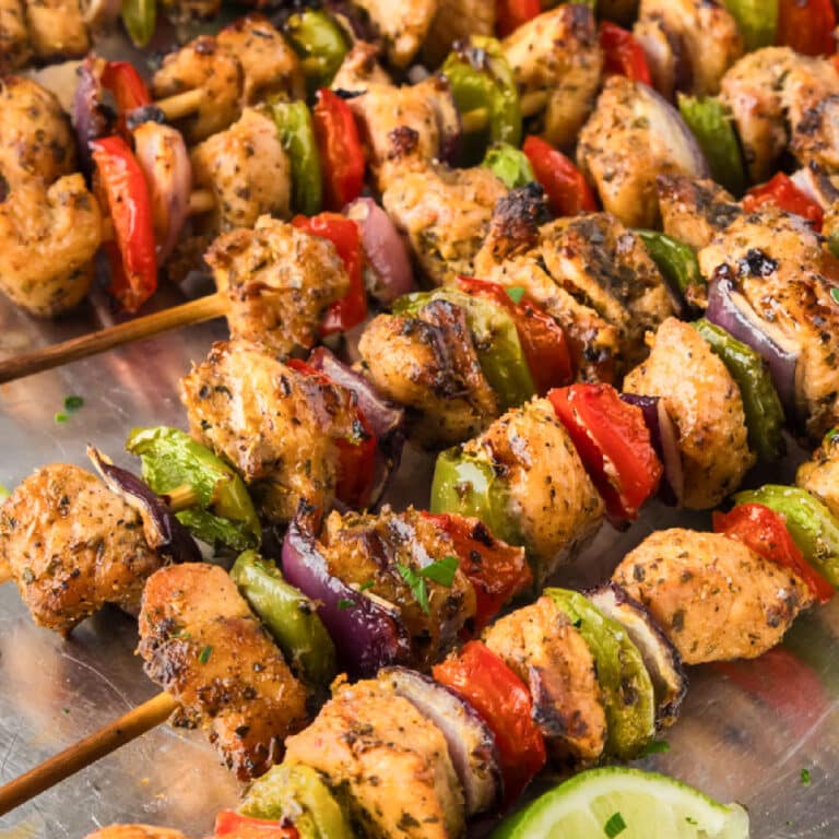 Close up square view of chicken fajita skewers piled on a serving platter.
