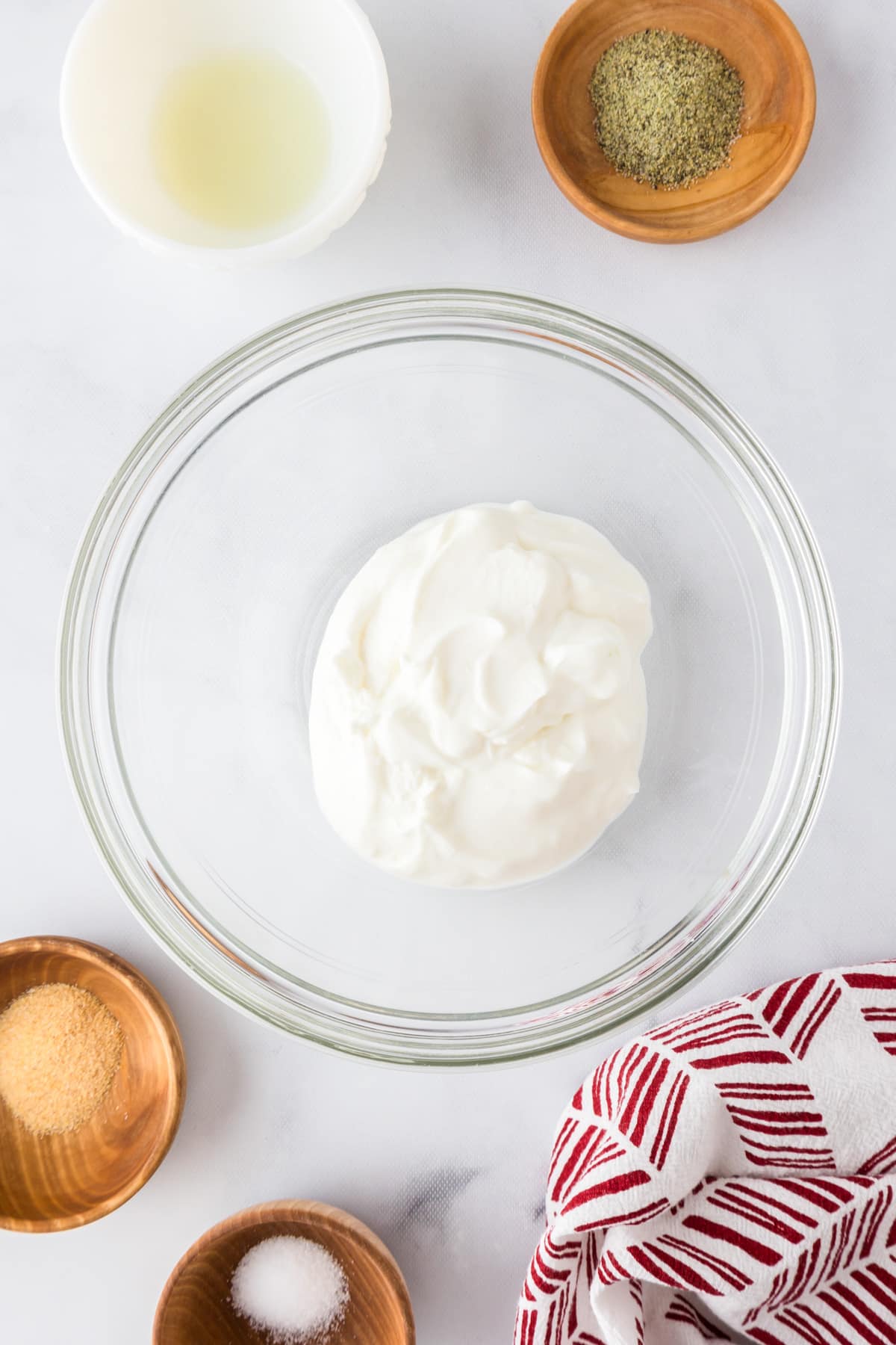 A glass bowl of plain greek yogurt surrounded by spices in small bowls.