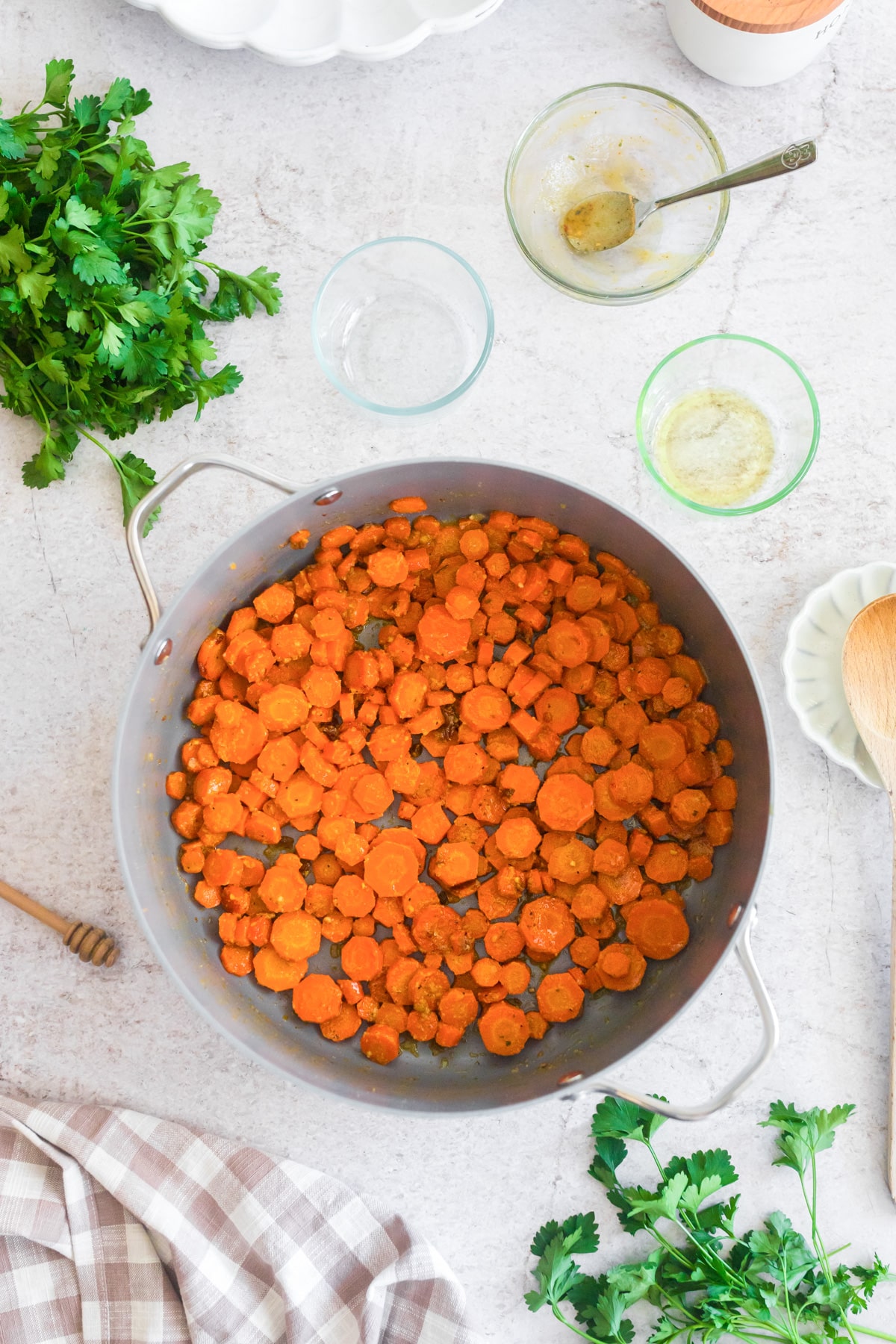 Sliced cooked honey mustard carrots in a large pot on a light countertop with empty bowls nearby.