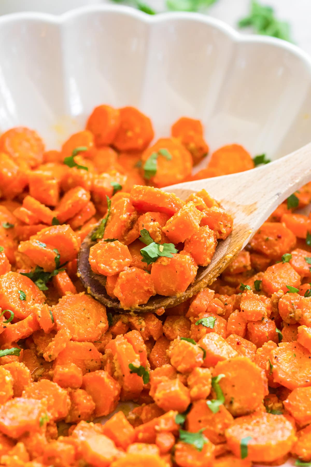 Sliced cooked honey mustard carrots carrots being scooped from a bowl.