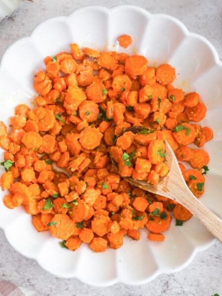 A bowl filled with sliced honey mustard carrots with a spoon scooping a serving.