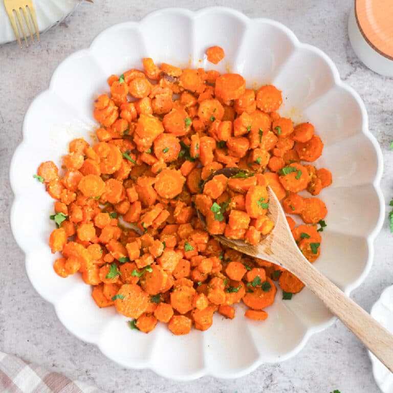 A bowl filled with sliced honey mustard carrots with a spoon scooping a serving.