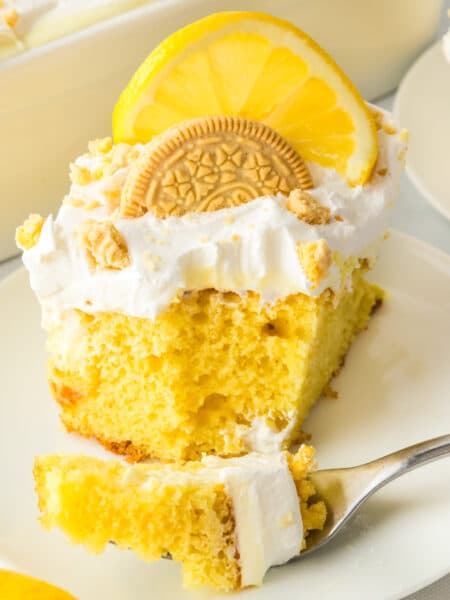 A slice of lemon poke cake on a plate with a bite missing and on a fork.