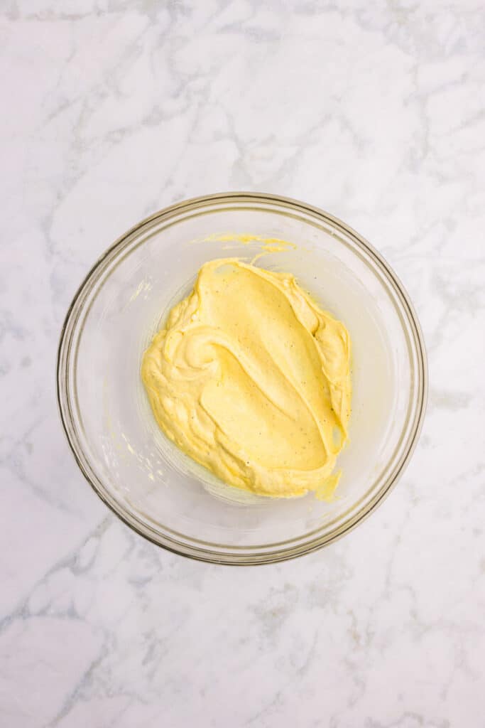 A glass bowl containing mayonnaise mixed with spices for chicken macaroni pasta salad.
