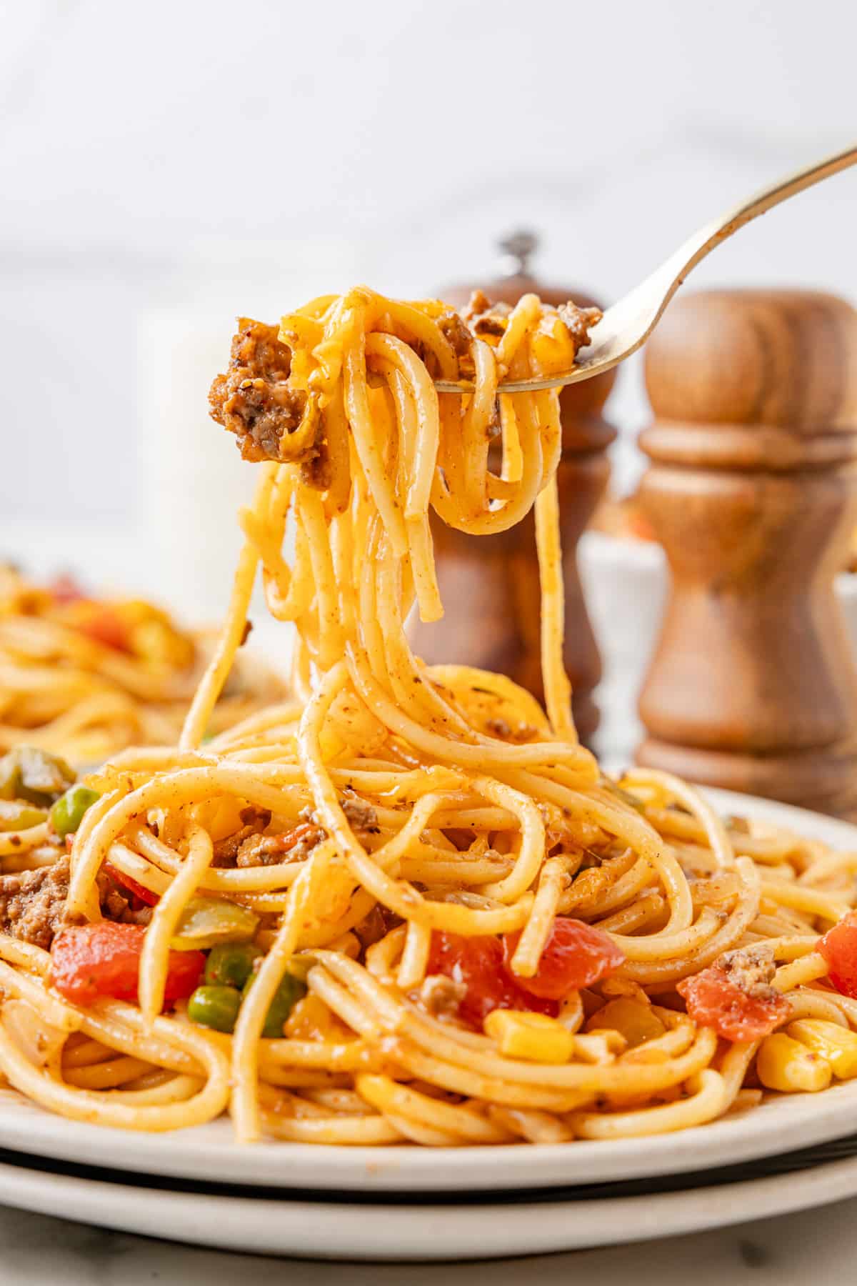 A fork lifting a serving of church supper spaghetti from a plate with ground meat, tomatoes, and peppers mixed with the pasta.