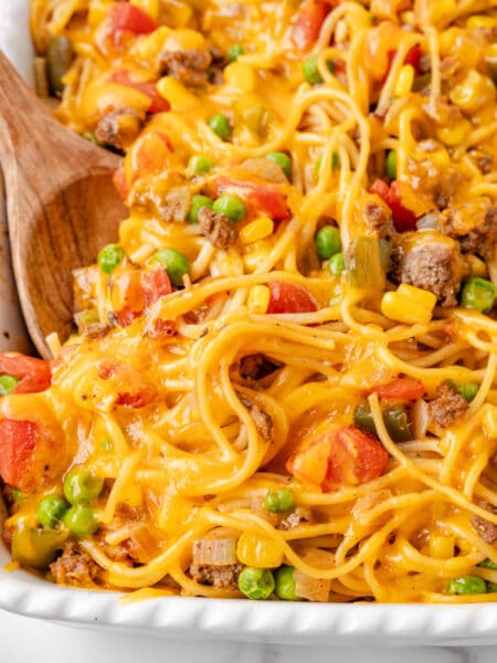 Close up square view of casserole dish filled with Church supper spaghetti mixed with ground beef, peas, corn, tomatoes, and melted cheddar cheese.