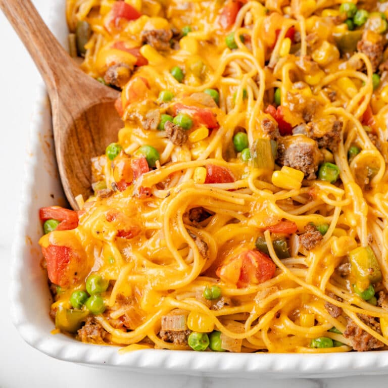 Close up square view of casserole dish filled with Church supper spaghetti mixed with ground beef, peas, corn, tomatoes, and melted cheddar cheese.
