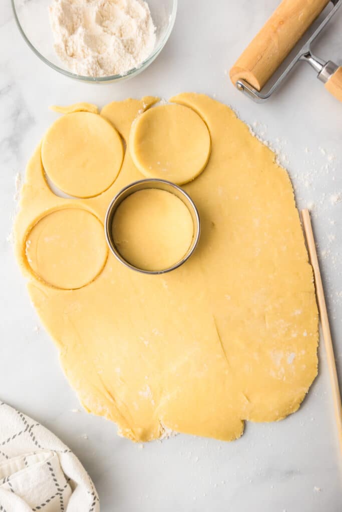 Rolled out sugar cookie dough cutting into cookies for fruit pizza cookies.