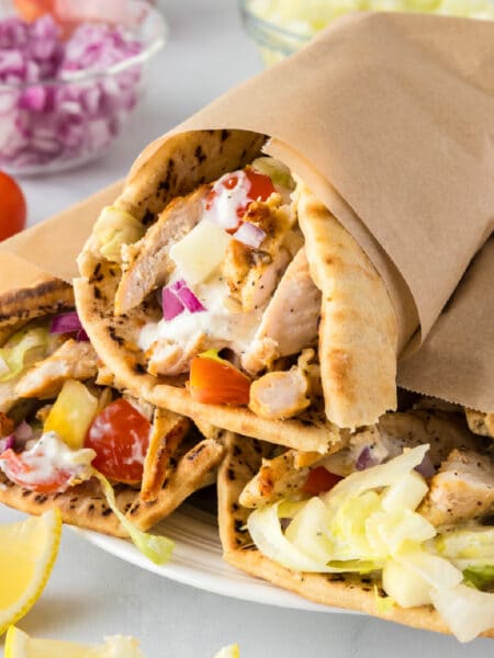 Three chicken wraps wrapped in pita bread with lettuce, tomatoes, onions, and greek yogurt sauce served on a platter.