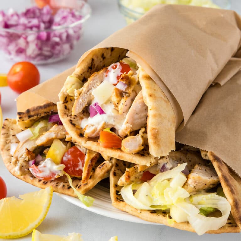 Three chicken wraps wrapped in pita bread with lettuce, tomatoes, onions, and greek yogurt sauce served on a platter.