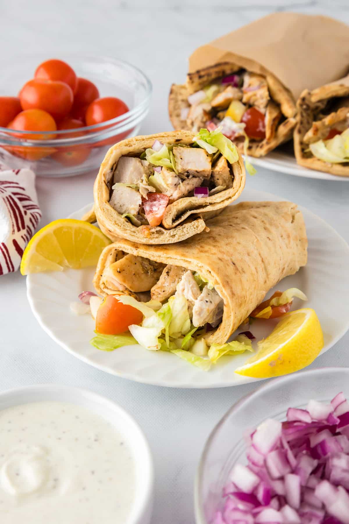 A plate with a greek wrap cut in half piled on a plate so you can see the chicken, lettuce and tomato with yogurt sauce filling.
