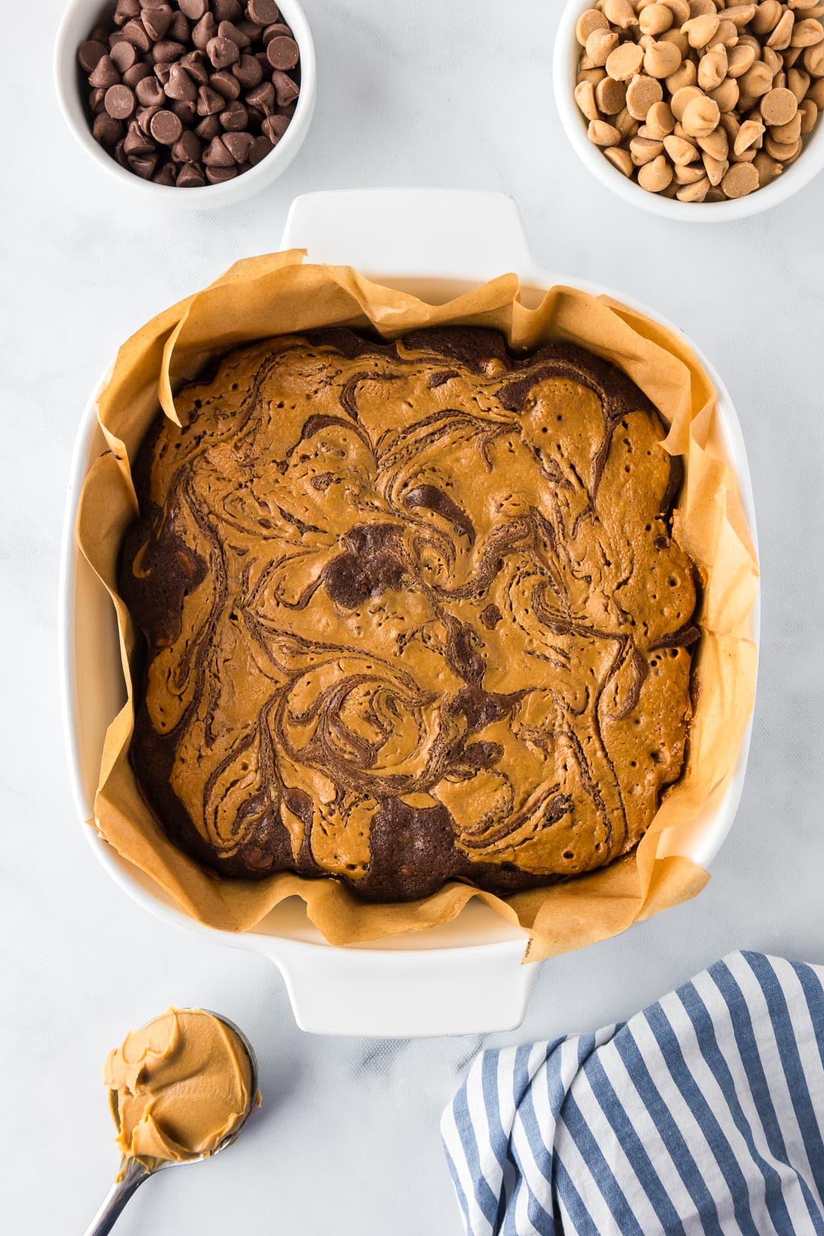 A square baking dish lined with parchment paper full of peanut butter swirled brownies.