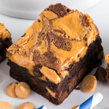 Close up view of a thick chocolate brownie with a swirled peanut butter topping, surrounded by a few peanut butter chips.