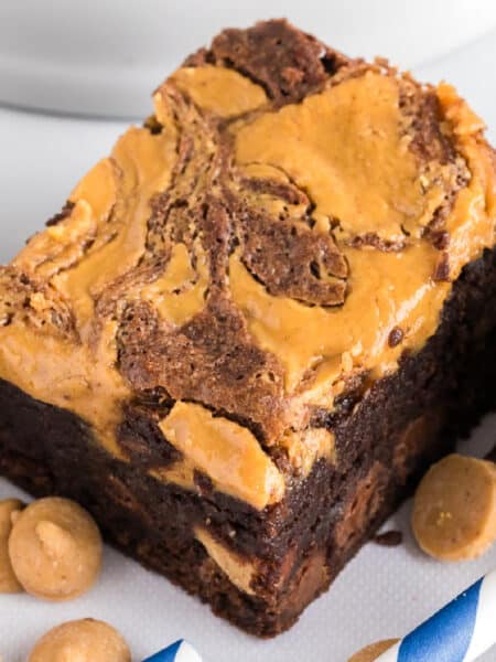 Close up view of a thick chocolate brownie with a swirled peanut butter topping, surrounded by a few peanut butter chips.