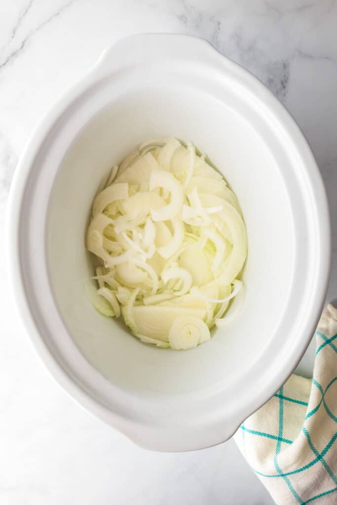 Sliced onions placed inside a white slow cooker.