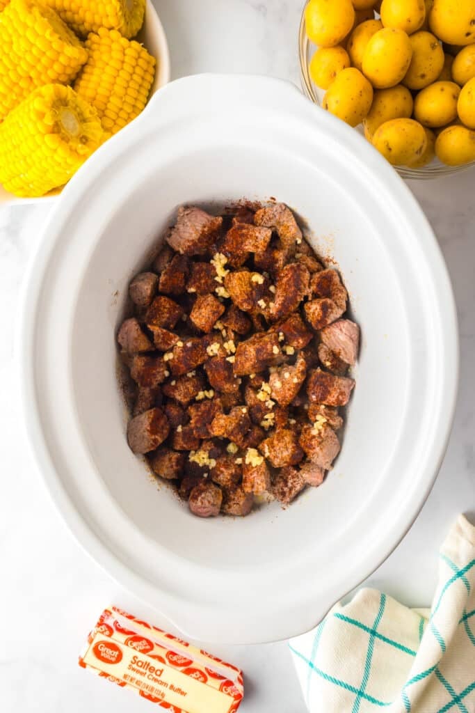 Chunks of seasoned steak in the bottom of a slow cooker.